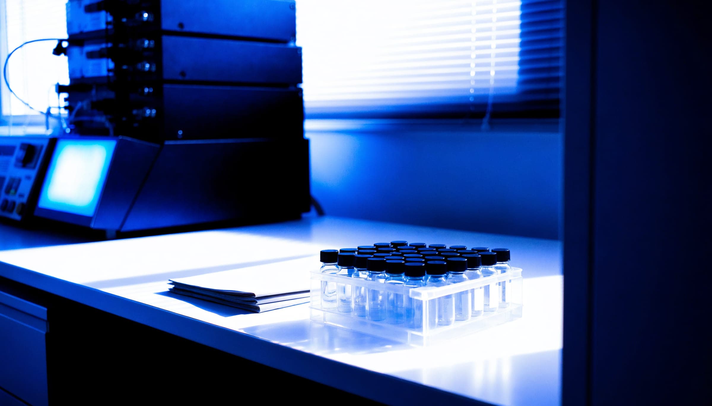 Banco de laboratorio iluminado en azul con un rack de viales durante el análisis